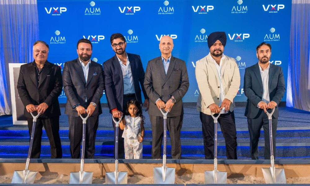 Business executives at groundbreaking ceremony holding silver shovels in front of VXP and AUM Development branded backdrop