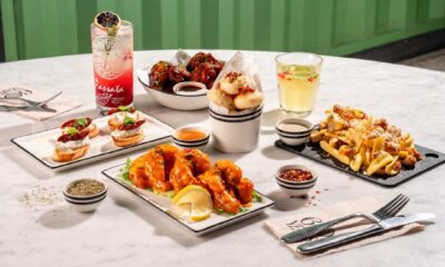 Assorted restaurant appetizers and cocktails including wings, sliders, fries, and colorful drinks on marble table
