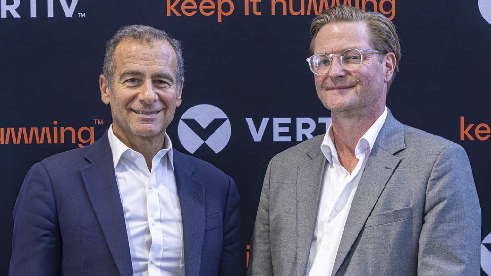 Two business executives at Vertiv press event with keep it humming branding