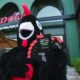 Barci, Nando's black and red rooster mascot, holding scratch-and-win cards outside Nando's JBR restaurant in Dubai