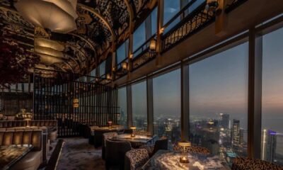 Luxury restaurant interior with ornate decorative ceiling, floor-to-ceiling windows, and panoramic Dubai cityscape views at twilight