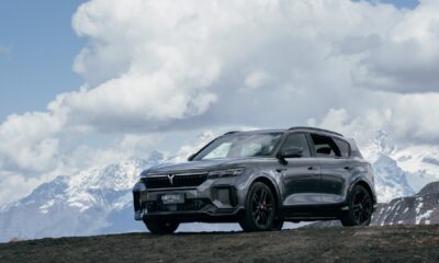 Dark gray SUV with black wheels positioned on mountain terrain with snow-capped peaks and cloudy sky in background