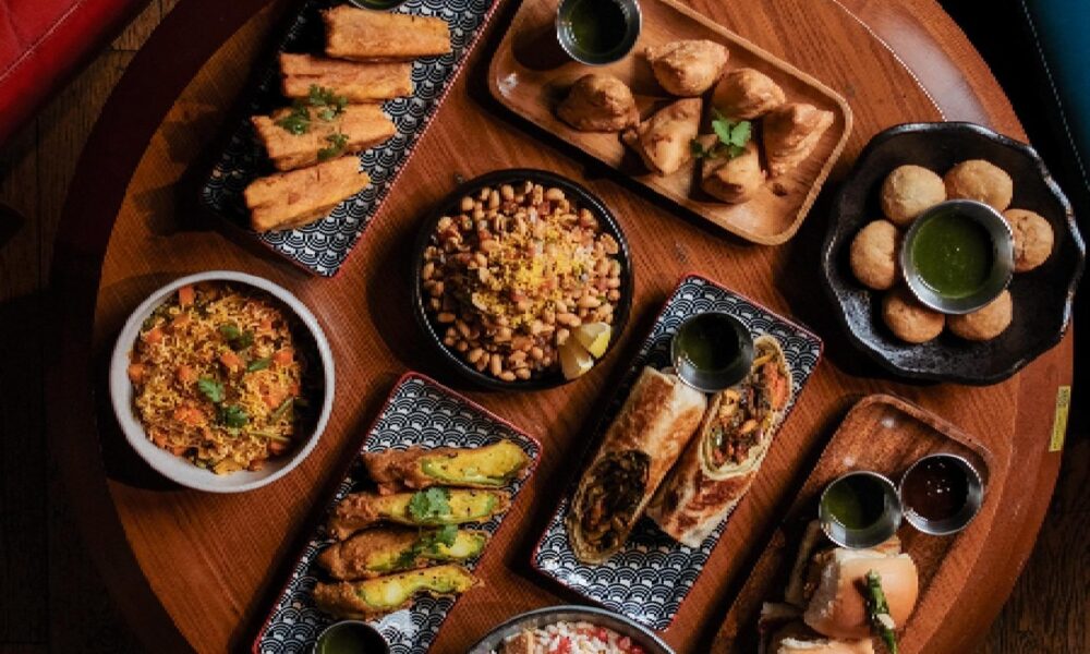 Overhead view of Indian appetizers and dishes including samosas, pakoras, rice, and chutneys on wooden serving boards