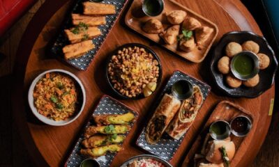 Overhead view of Indian appetizers and dishes including samosas, pakoras, rice, and chutneys on wooden serving boards