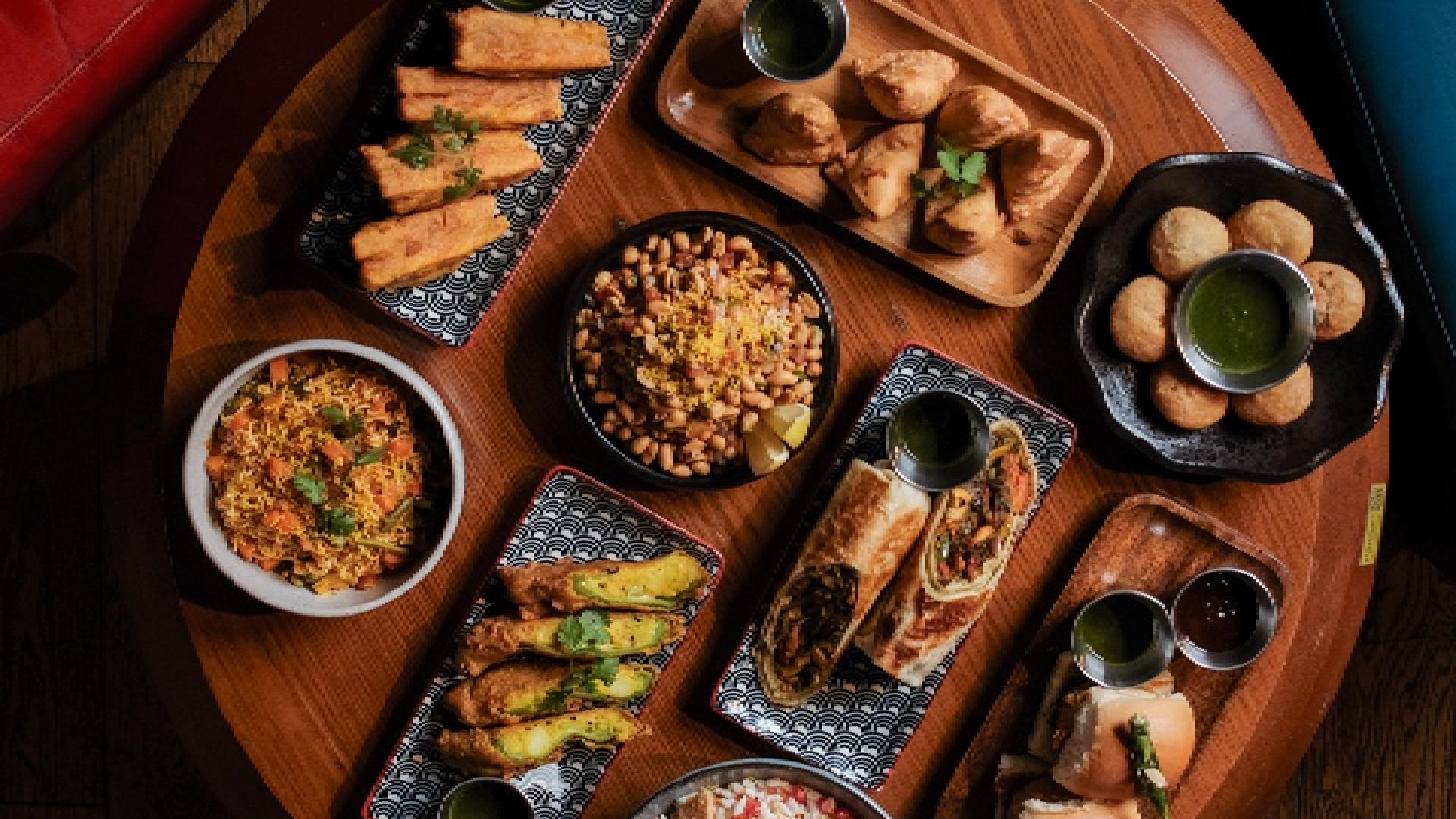 Overhead view of Indian appetizers and dishes including samosas, pakoras, rice, and chutneys on wooden serving boards
