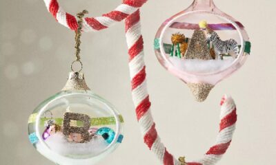 Whimsical glass Christmas ornaments with miniature winter scenes hanging from red and white striped ribbons