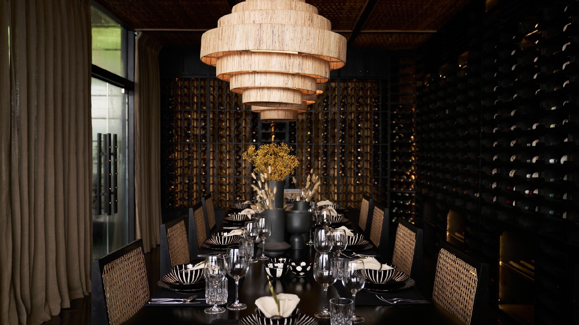 Elegant dining room at Sun Siyam Pasikudah with tiered woven chandelier, wicker chairs, and wine cellar wall