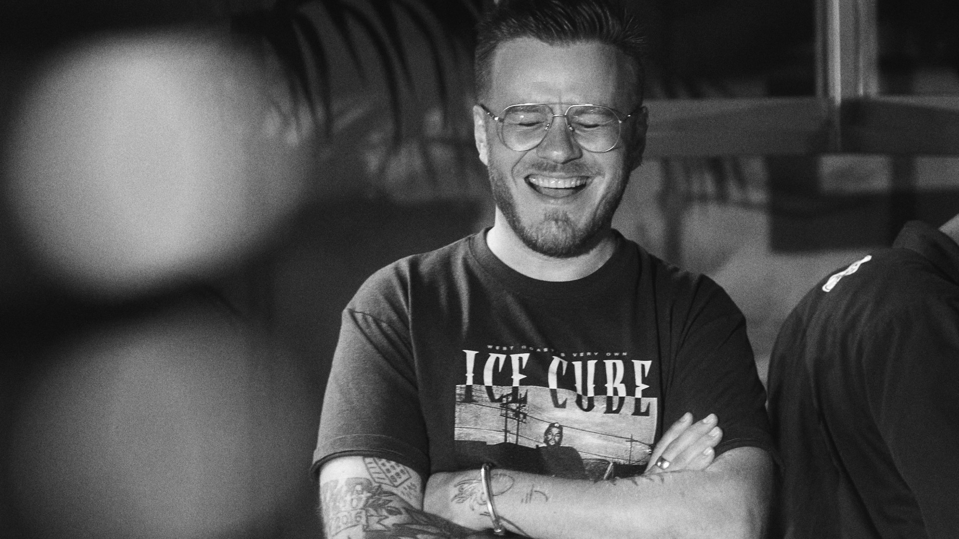 Smiling man wearing glasses and Ice Cube t-shirt in black and white photo at indoor venue