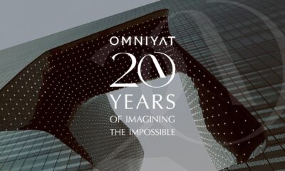 OMNIYAT 20 Years anniversary graphic overlaid on modern architectural building with illuminated facade featuring curved glass and geometric pattern
