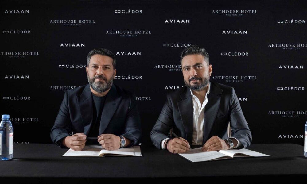 Two business executives signing partnership agreement at press conference with Aviaan, Clé d'Or, and Arthouse Hotel branding