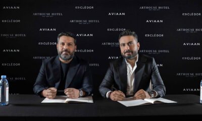 Two business executives signing partnership agreement at press conference with Aviaan, Clé d'Or, and Arthouse Hotel branding