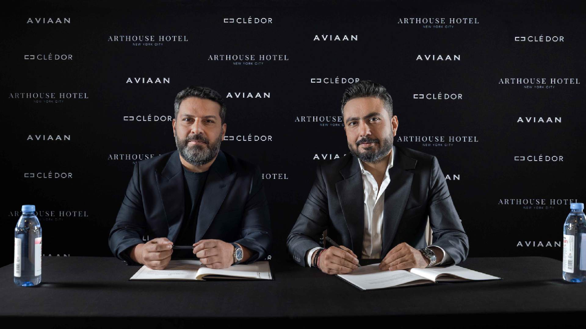 Two business executives signing partnership agreement at press conference with Aviaan, Clé d'Or, and Arthouse Hotel branding