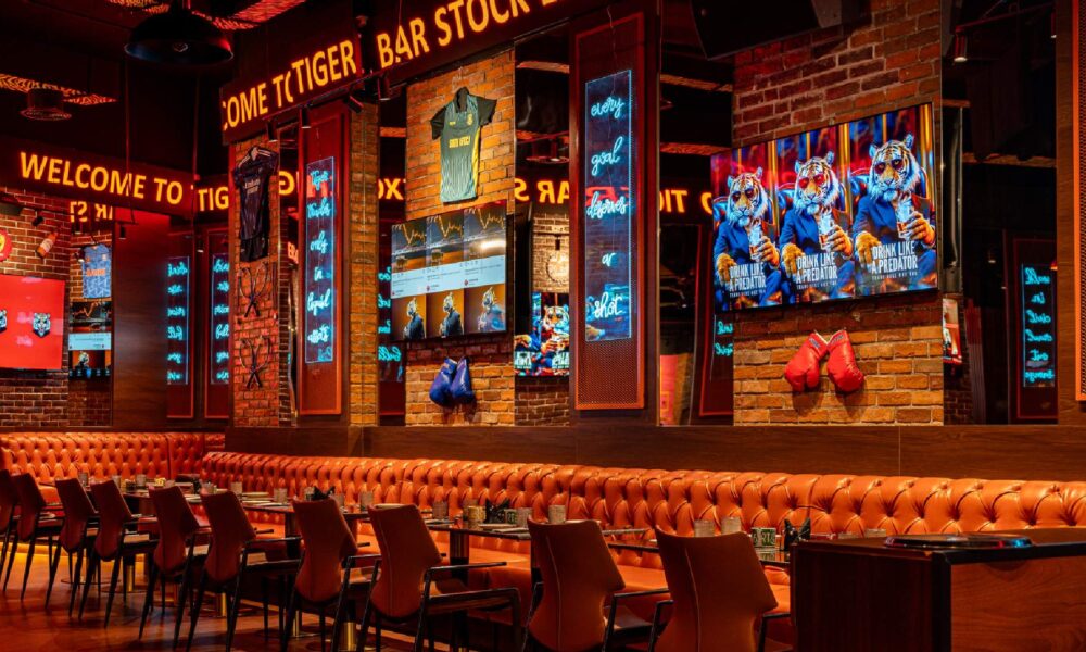 Tiger Bar Stock Exchange interior with neon signs, orange leather seating, sports memorabilia, and multiple screens at Barceló Al Jaddaf
