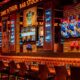 Tiger Bar Stock Exchange interior with neon signs, orange leather seating, sports memorabilia, and multiple screens at Barceló Al Jaddaf
