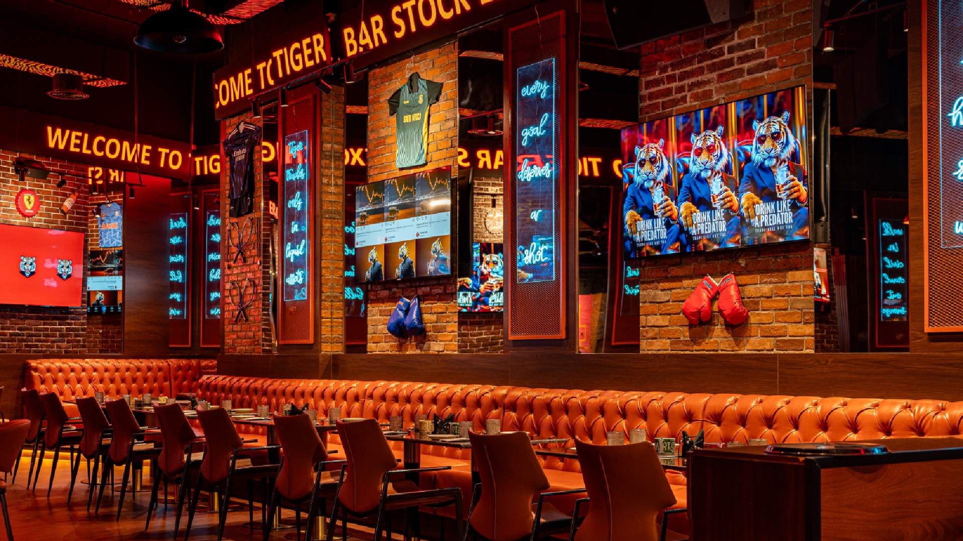 Tiger Bar Stock Exchange interior with neon signs, orange leather seating, sports memorabilia, and multiple screens at Barceló Al Jaddaf