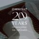OMNIYAT 20 Years anniversary graphic overlaid on modern architectural building with illuminated facade featuring curved glass and geometric pattern