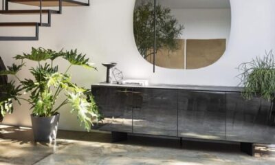 A luxurious, light-filled living room features a modular, pale beige sofa, a low wooden coffee table with books and decor, and a soft, patterned area rug, emphasizing comfort and minimalist Italian design.