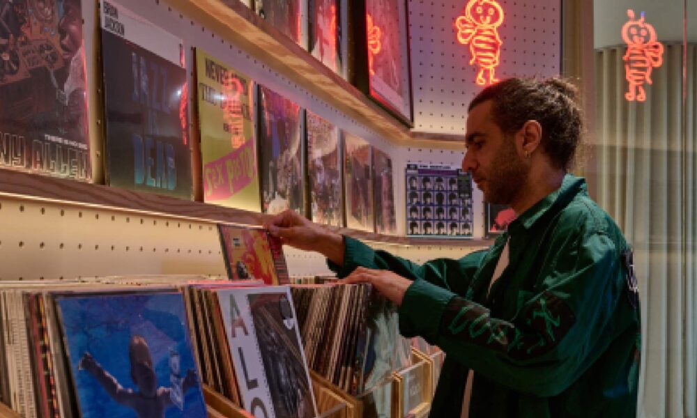 Young man browsing vinyl records and posters in retro music store with neon lighting