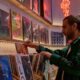 Young man browsing vinyl records and posters in retro music store with neon lighting