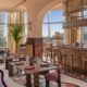 SO/ Ras Al Khaimah restaurant interior featuring warm earth tones, decorative bar area, and floor-to-ceiling windows with natural light