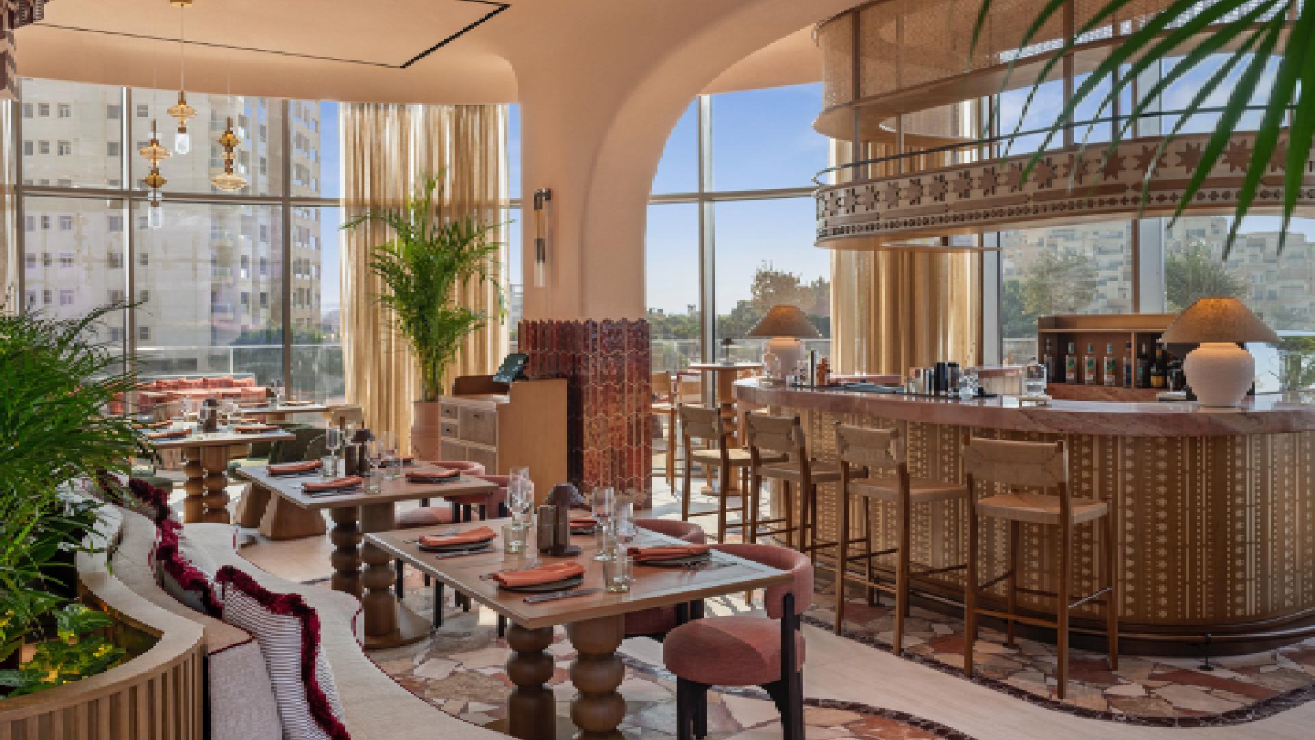 SO/ Ras Al Khaimah restaurant interior featuring warm earth tones, decorative bar area, and floor-to-ceiling windows with natural light