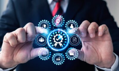 Businessman in suit holding holographic digital icons representing quality management systems including gears, checkmark, security, analytics, and team collaboration symbols
