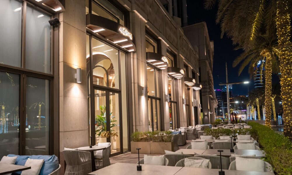 "Luxury outdoor dining terrace at night with modern architecture, ambient lighting, white seating, and illuminated palm trees in Dubai