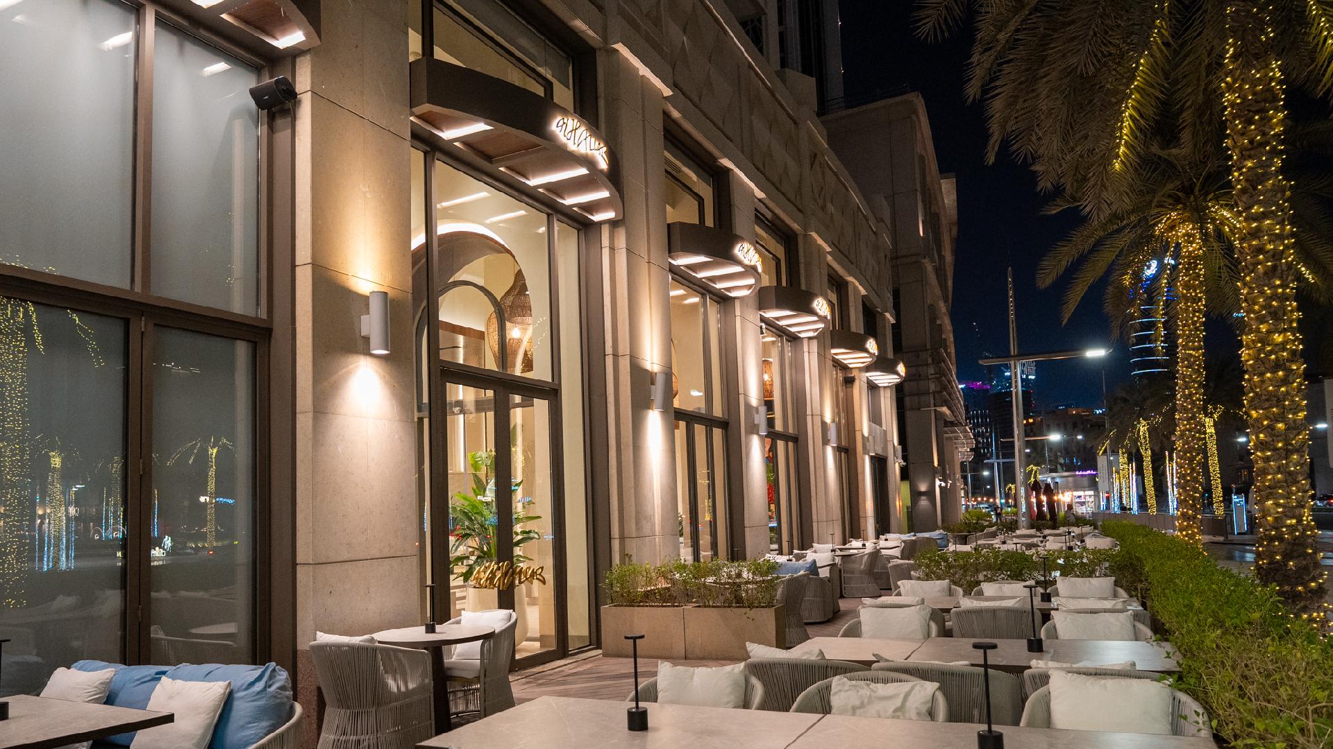 "Luxury outdoor dining terrace at night with modern architecture, ambient lighting, white seating, and illuminated palm trees in Dubai
