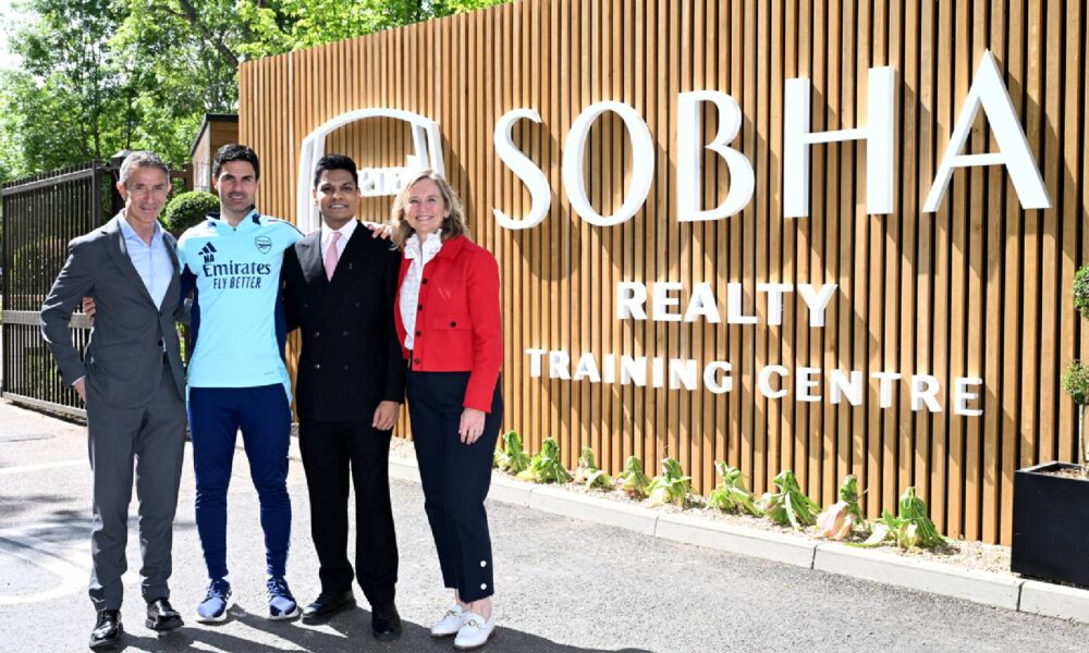 Four professionals standing in front of Sobha Realty Training Centre wooden signage with greenery
