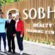 Four professionals standing in front of Sobha Realty Training Centre wooden signage with greenery