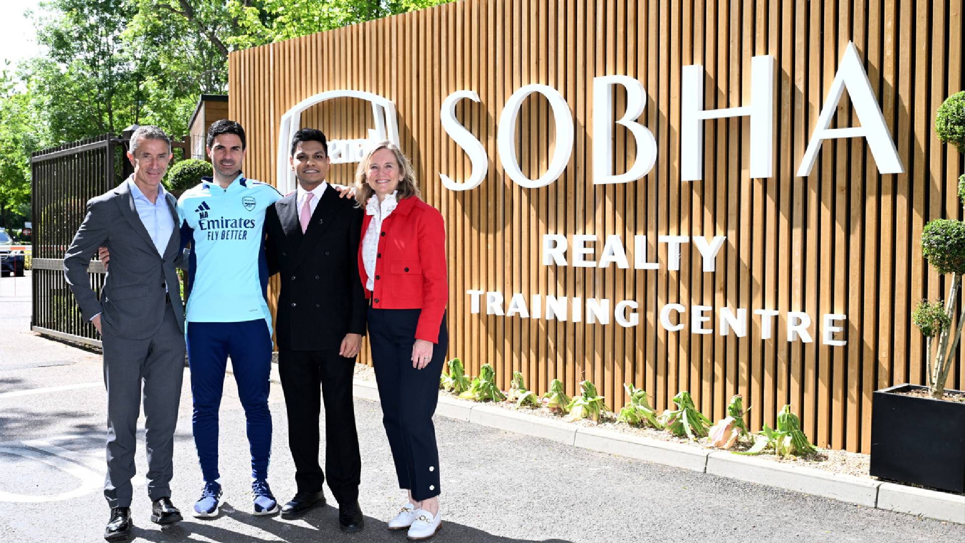 Four professionals standing in front of Sobha Realty Training Centre wooden signage with greenery