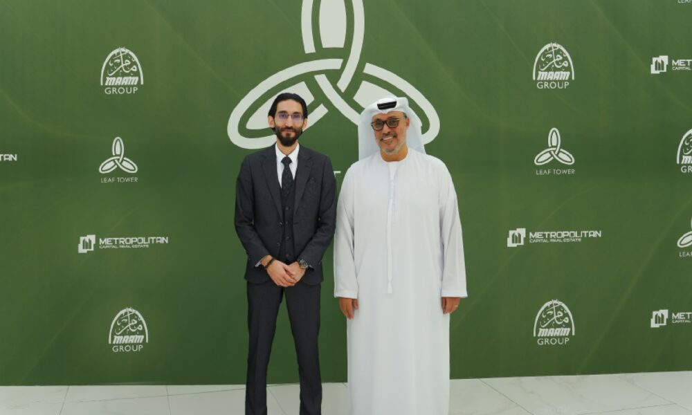 Two business professionals pose at a corporate event with green branded backdrop featuring Metropolitan, Manarah Group, and Leaf Tower logos