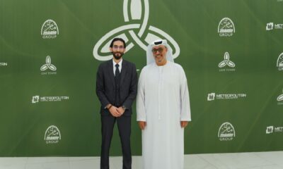 Two business professionals pose at a corporate event with green branded backdrop featuring Metropolitan, Manarah Group, and Leaf Tower logos