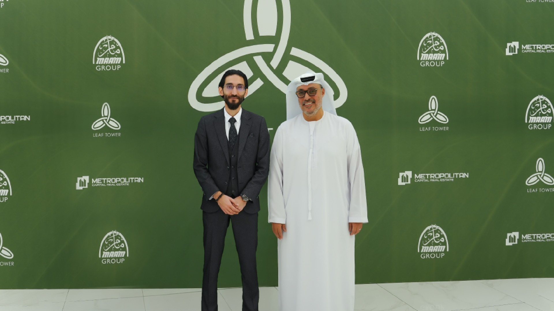 Two business professionals pose at a corporate event with green branded backdrop featuring Metropolitan, Manarah Group, and Leaf Tower logos