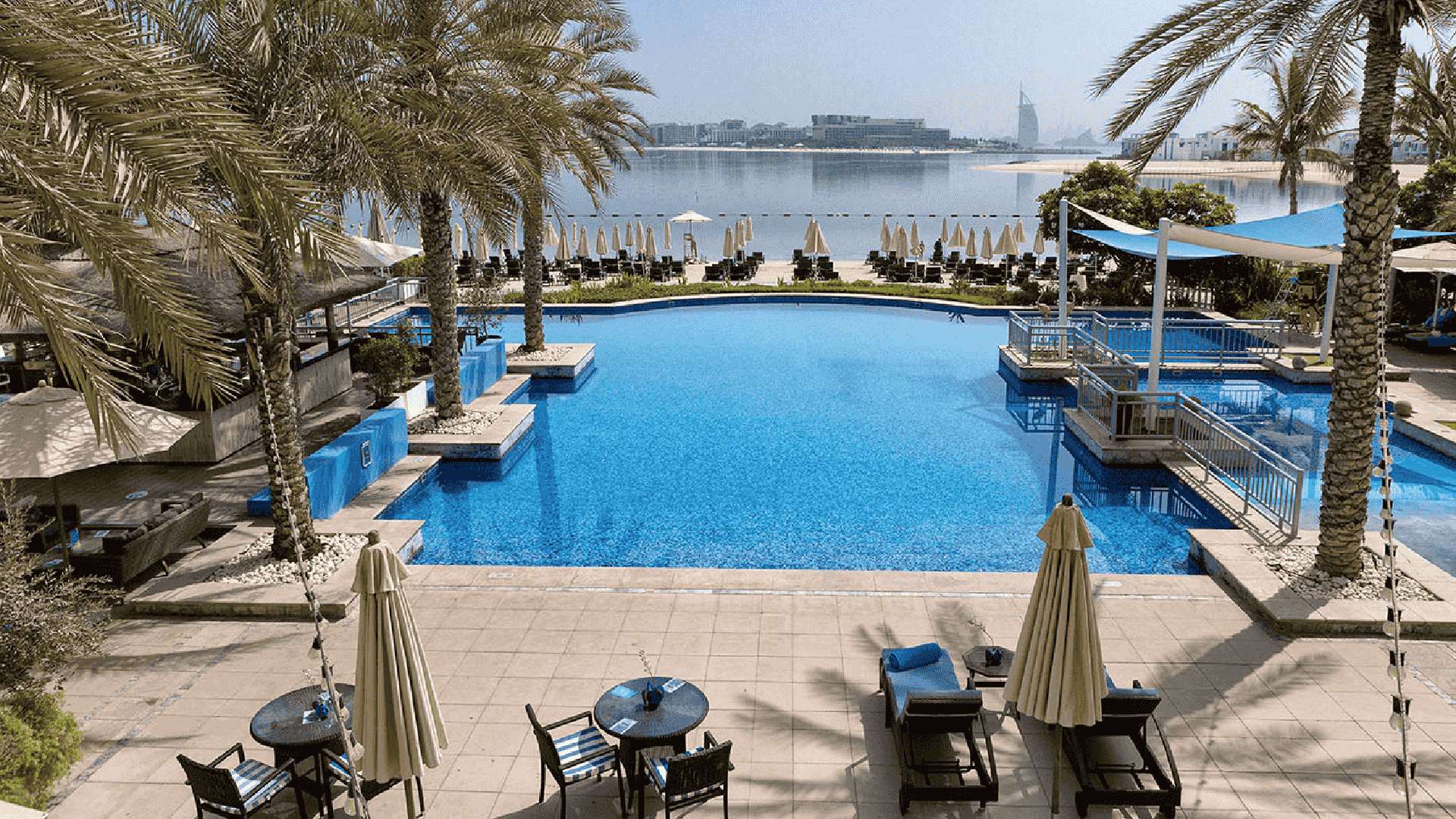 RIVA Beach Club swimming pool with palm trees overlooking Palm Jumeirah beach and Dubai skyline with Burj Al Arab view