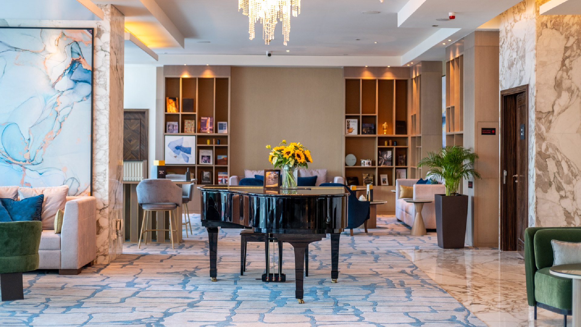 Authors' Lounge interior at voco Bonnington Dubai featuring grand piano, elegant seating, bookshelves, and crystal chandeliers