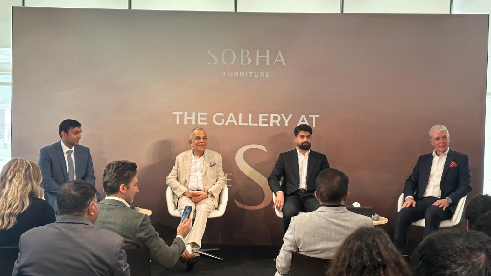 A modern showroom interior displays various kitchen and wardrobe modules under bright directional lighting, featuring dark wood cabinets, contrasting light stone countertops, and sleek, minimalist design.