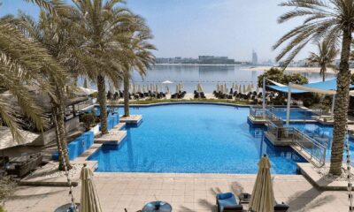 Infinity pool overlooking beach and Dubai skyline with palm trees and sun loungers at beachfront resort