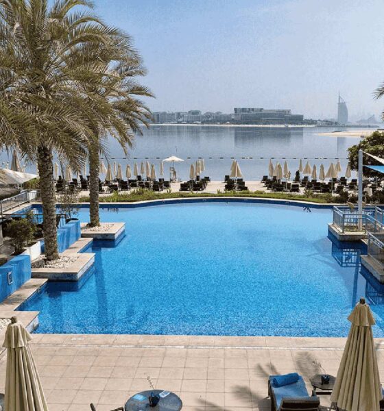 Infinity pool overlooking beach and Dubai skyline with palm trees and sun loungers at beachfront resort