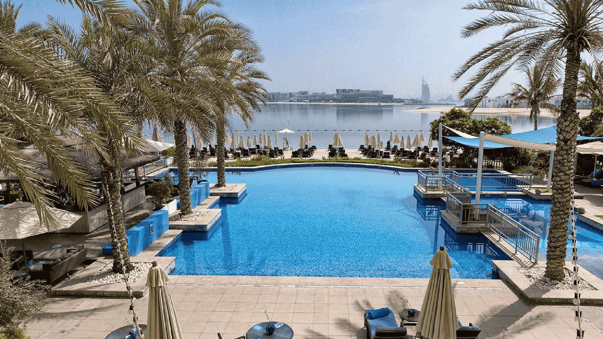 Infinity pool overlooking beach and Dubai skyline with palm trees and sun loungers at beachfront resort
