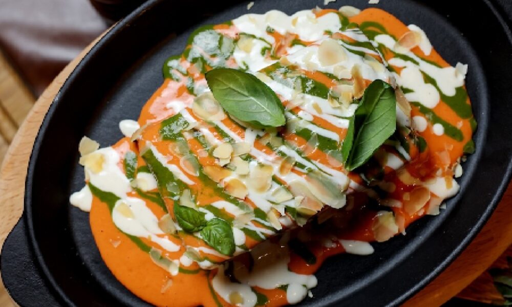 Gourmet dish with creamy sauce, fresh basil leaves, and shredded cheese on a black plate