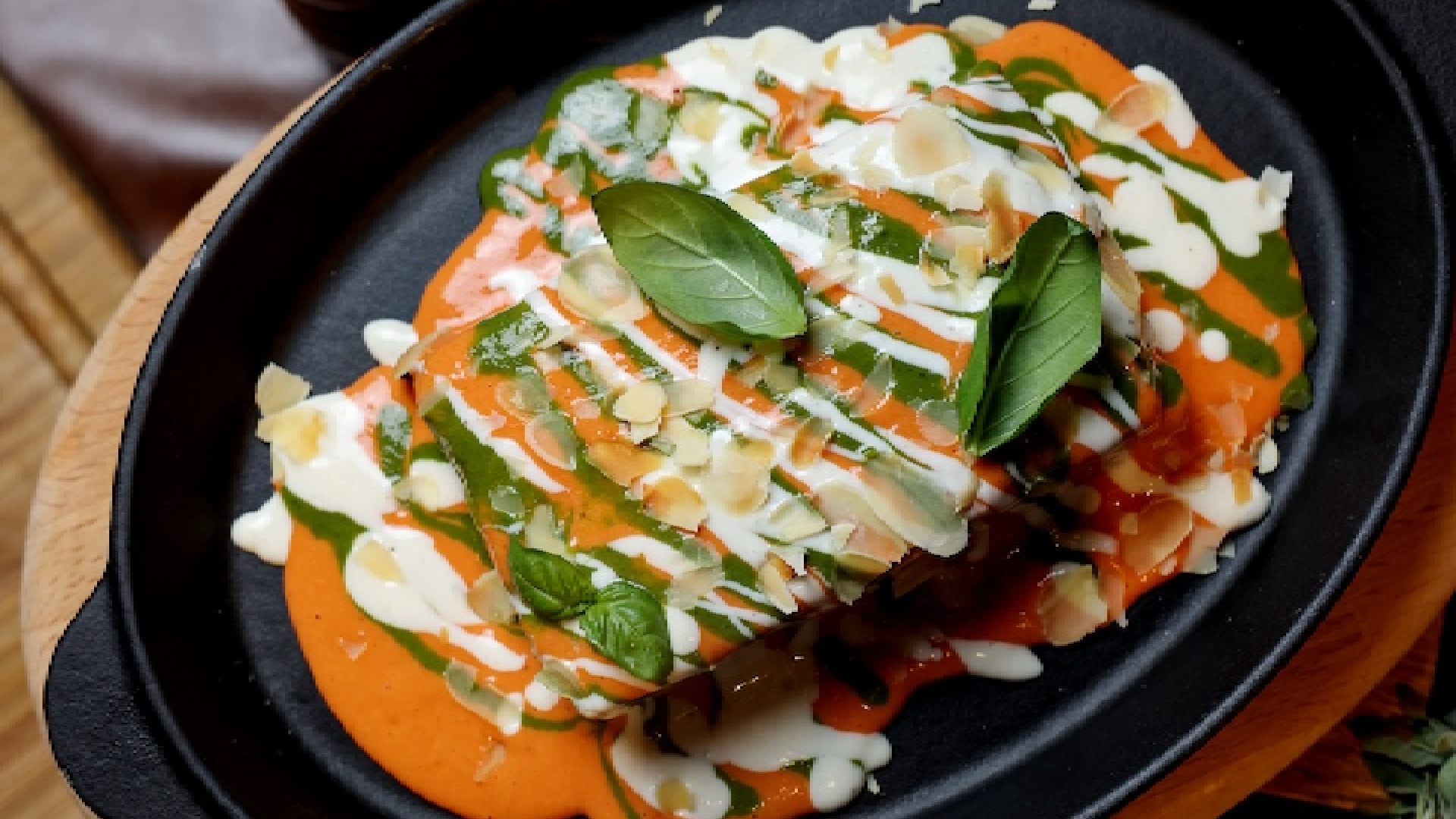 Gourmet dish with creamy sauce, fresh basil leaves, and shredded cheese on a black plate