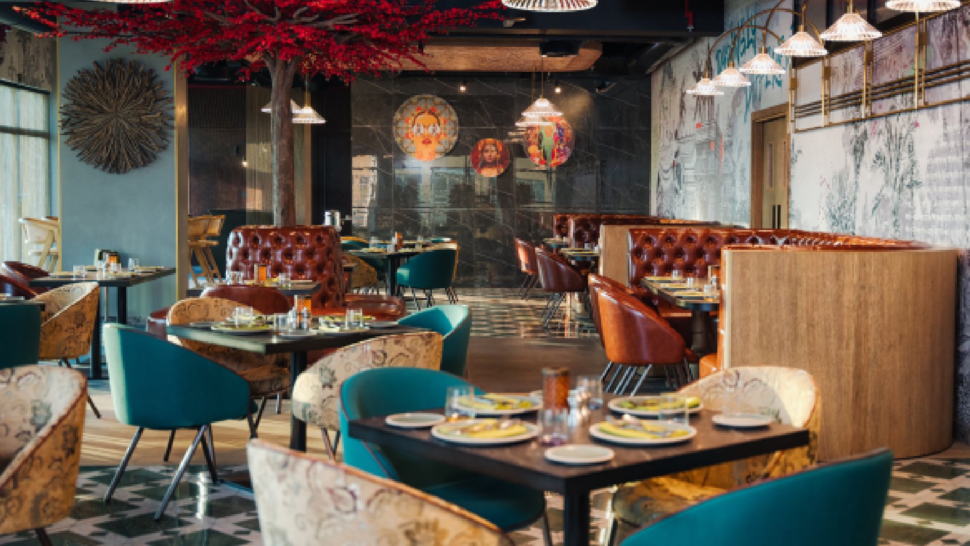 Rohini restaurant interior at Mövenpick JLT featuring colorful seating, Indian artwork, decorative tree, and modern dining ambiance