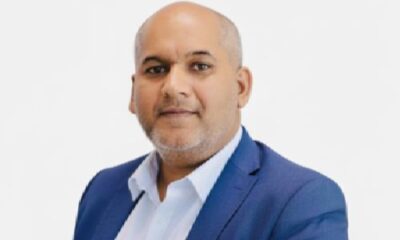 Professional headshot of a bald man with a grey beard wearing a blue suit jacket and white shirt against a light grey background