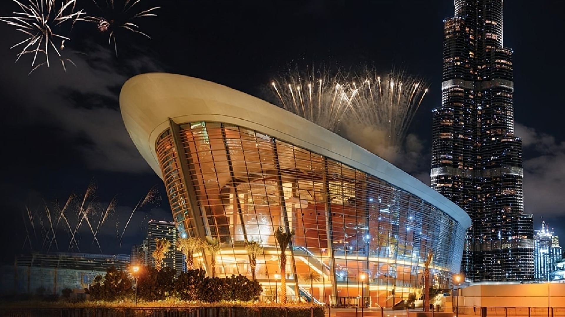 A luxurious, well-lit restaurant interior features a large white stone counter with high stools, modern minimalist decor, and a wall of geometric shelving holding decorative vases and art.
