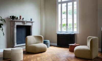 A modern living room features a large, dark brown leather sofa with a chaise lounge, light wood flooring, and a glass-topped coffee table, with a partial view of a dining area in the background.