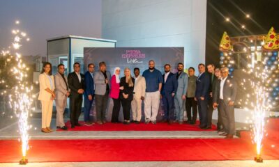 A small, minimalist desk area features a large, simple mirror, a contemporary light fixture, and a decorative vase, set against a dark-paneled wall and a white countertop.
