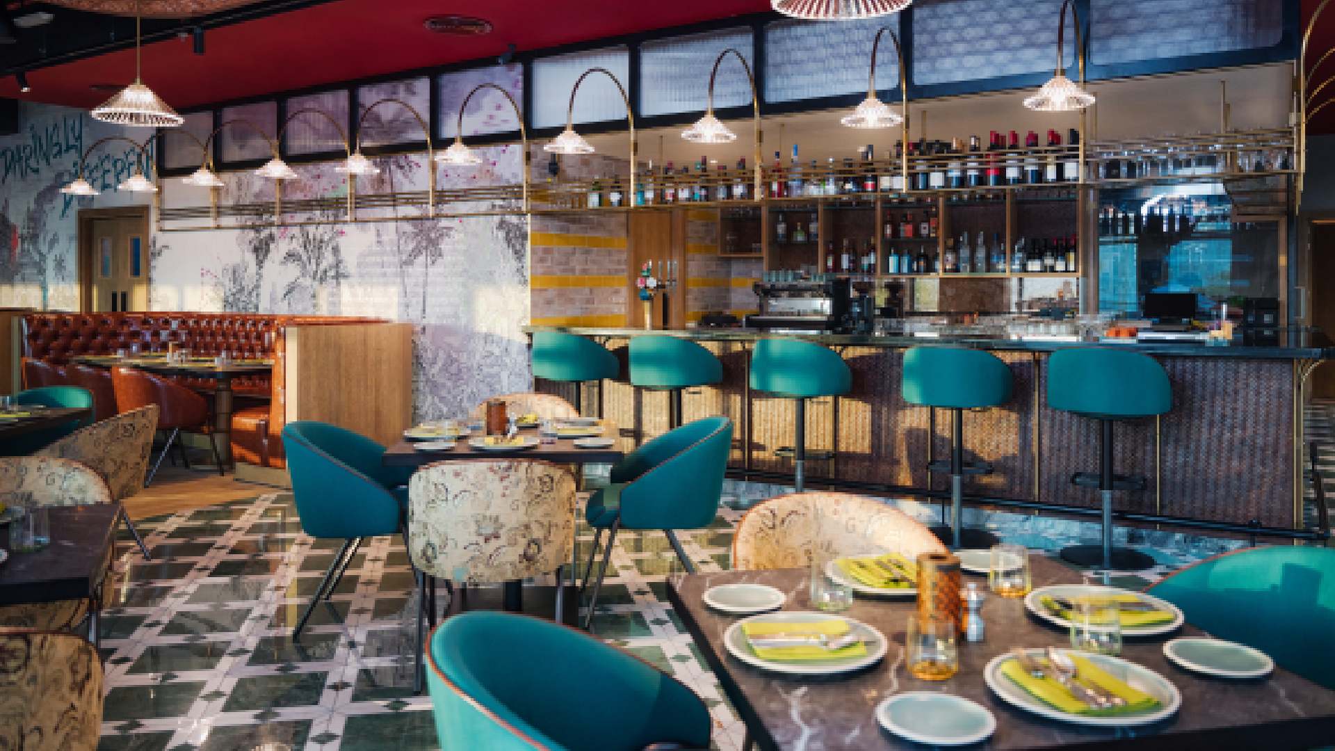 A modern Indian restaurant interior features dark wooden ceilings and seating, geometric patterned dividers, and decorative brass lanterns hanging above a row of banquette seating.