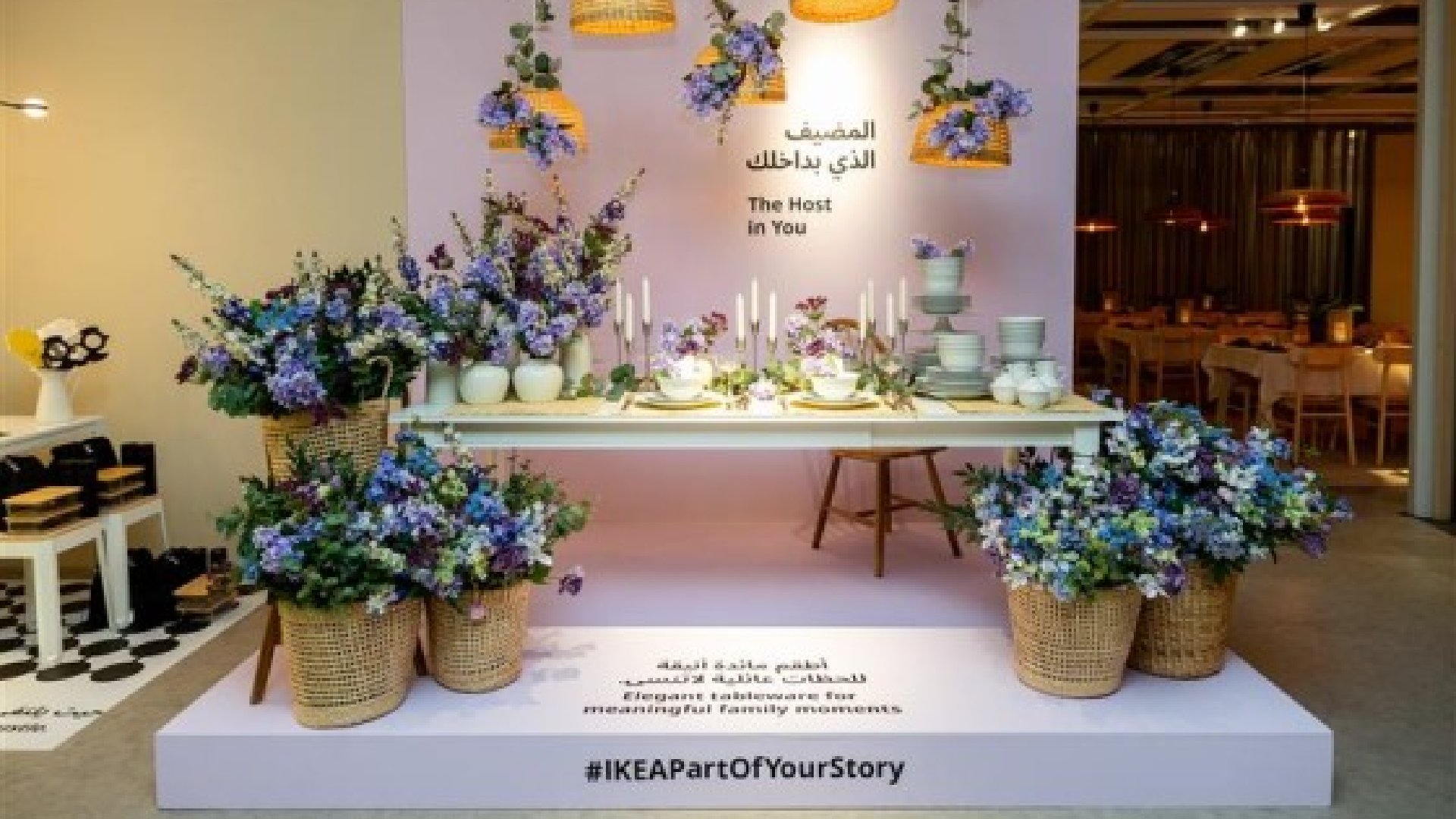 A white, modern apartment interior features a light-colored sectional sofa, a black-framed glass partition separating the living space from another room, and a decorative tree in the corner.