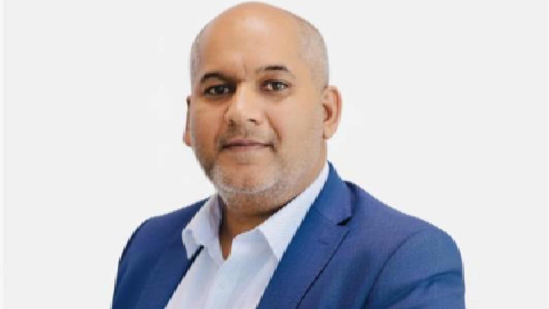 Professional headshot of a bald man with a grey beard wearing a blue suit jacket and white shirt against a light grey background